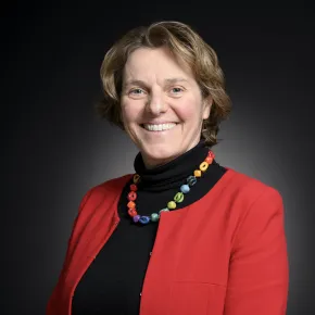 headshot of woman in a red jacket against a dark background