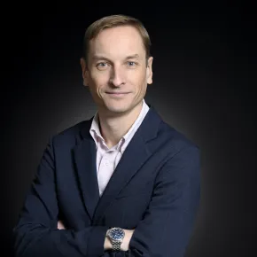 headshot of man in dark suit against black background