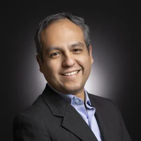 headshot of man in dark suit against black background