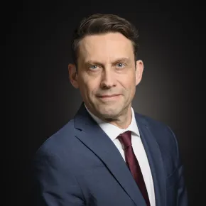 headshot of man in gray suit against dark background
