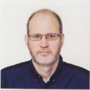 headshot of man in glasses and dark shirt against a white background