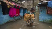 an indian woman holding her pet dog as she walks through a flooded street