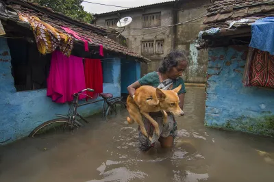 an indian woman holding her pet dog as she walks through a flooded street