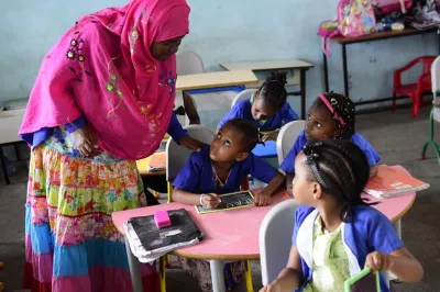 a female teacher leans over the desk of a pupil in a classroom 