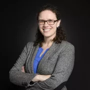 headshot of woman in gray blazer against dark backrgound