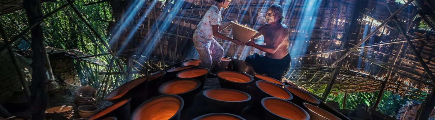 oung person with an elderly person creating ceramics under a wood-built shelter