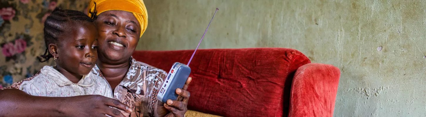 a mother and young daughter sit on a sofa listening to a portable radio
