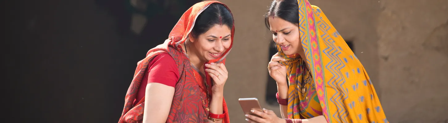 two women in colorful Indian national dress look at a smartphone