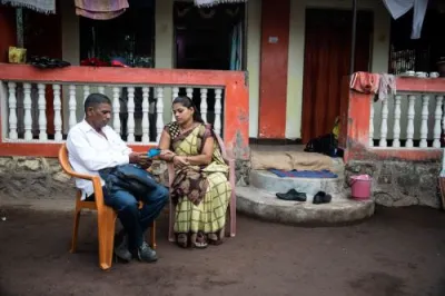 a male collects a deposit from a female client as they sit in front of a home in india