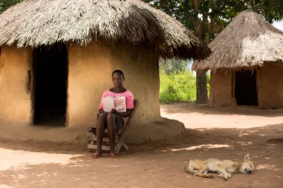 A young woman sits outside her home reading with a dog sleeping in the foreground