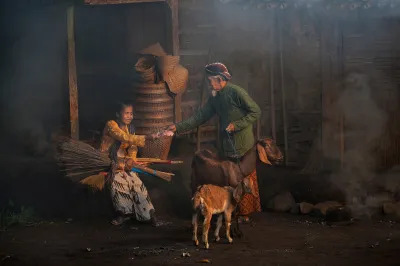A rural couple and their goat in Indonesia sit in a dark barn