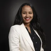 headshot of woman in white jacket against dark background