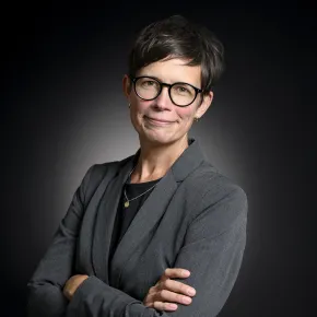 headshot of woman in gray jacket against dark background