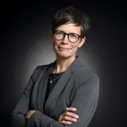 headshot of woman in gray jacket against dark background
