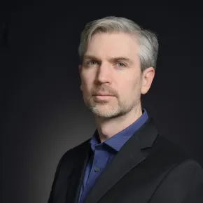 headshot of man in dark suit against black background
