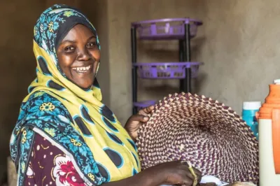an African woman chopping coconuts smiling at camera