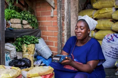 An african woman sits in front of a market making a digital payment