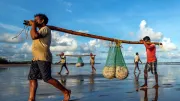 Fishermen walk the beach with their catch in India